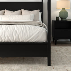 Modern black four-poster bed with white linens, beige throw pillows, black nightstand, green table lamp and neutral area rug