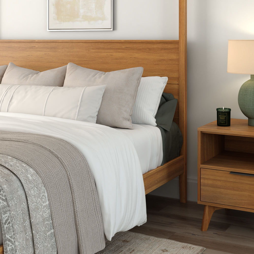Cozy bedroom with wooden bed frame, white bedding, and decorative pillows, featuring a wooden nightstand with a modern lamp and candle.