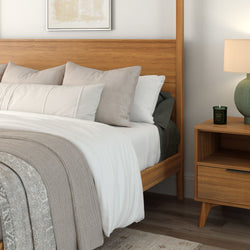 Cozy bedroom with wooden bed frame, white bedding, and decorative pillows, featuring a wooden nightstand with a modern lamp and candle.