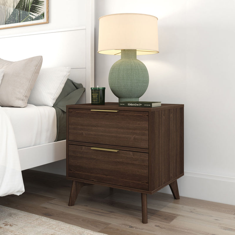 Mid-century modern walnut nightstand bedside table with two drawers and brass handles beside a white bed, styled with a green textured table lamp, scented candle and book on light hardwood floor