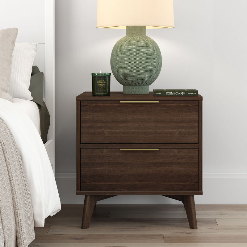 Mid-century modern dark walnut two-drawer nightstand with brass handles topped with a green textured table lamp, patchouli scented candle and book next to a white bed in a minimalist bedroom