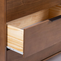 Close-up of a solid wood dresser drawer showing natural pine interior, brown stained front panel, white metal drawer slide and matte black handle