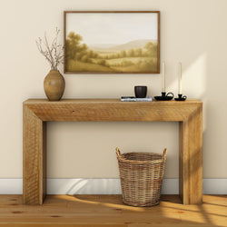 Modern living room with a wooden console table, decorative vase, candles, and wicker basket, featuring a landscape painting.