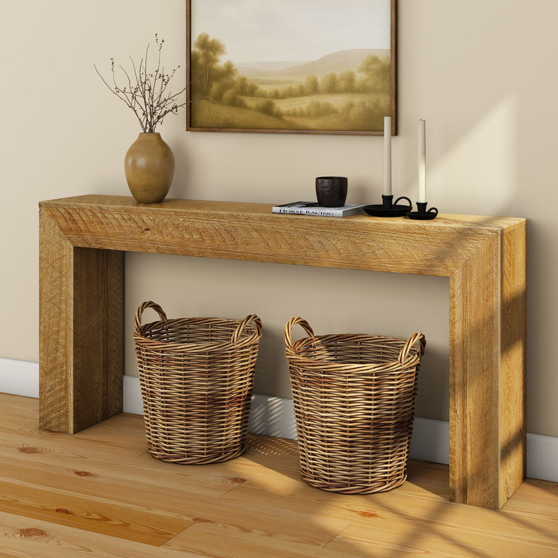 Rustic wooden console table with two woven wicker baskets underneath, neutral landscape wall art, ceramic vase with dried branches and black candle holders on hardwood floor