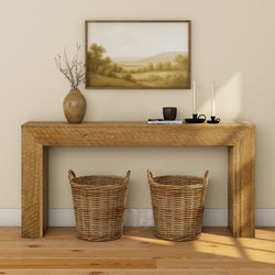 Rustic wooden console table in a neutral entryway with two woven wicker baskets underneath, ceramic vase with branches, black candle holders and framed landscape painting, modern farmhouse home decor