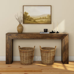 Rustic wooden console table in neutral entryway with framed landscape painting, ceramic vase, tapered candles and two wicker baskets on hardwood floor