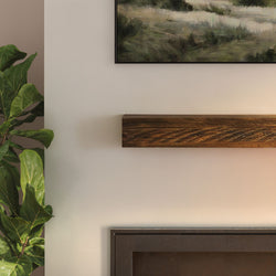 Modern living room close-up with rustic floating wooden mantel above minimalist fireplace, fiddle leaf fig plant and framed landscape art on a neutral wall