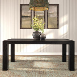 Black wood dining table with decorative ceramic vases and green foliage under a woven rattan pendant light, framed abstract art on a neutral shiplap wall and textured area rug