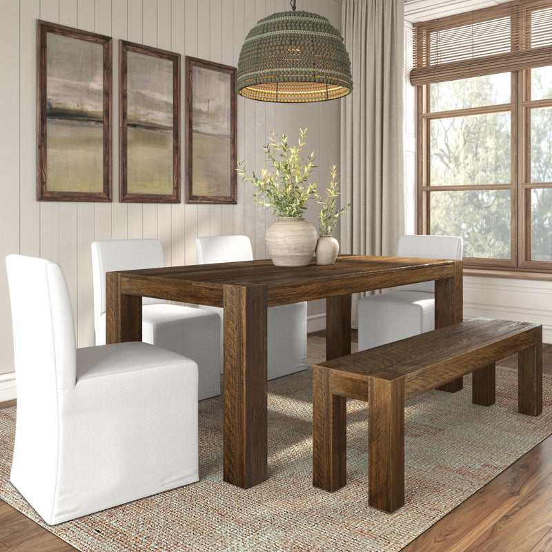 Rustic farmhouse dining room with reclaimed solid wood dining table and bench, white slipcovered chairs, woven pendant light, neutral artwork, large wood-framed window, and textured area rug