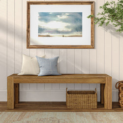Minimalist wooden bench with decorative pillows and framed artwork on white shiplap wall.