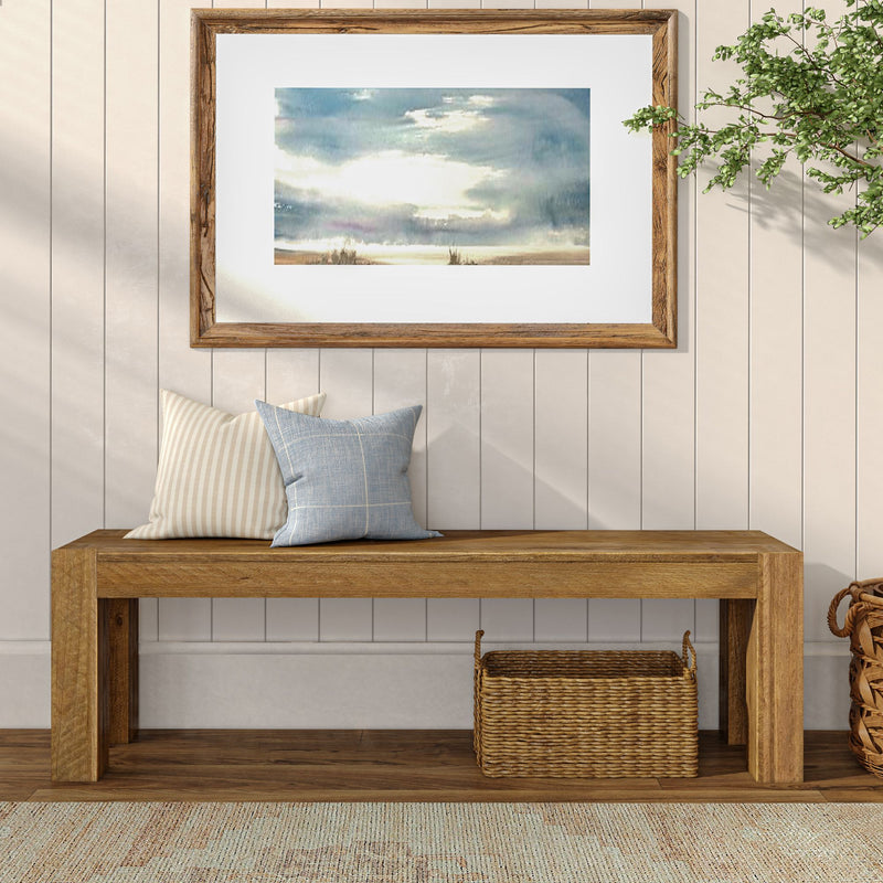 Minimalist wooden bench with decorative pillows and framed artwork on white shiplap wall.