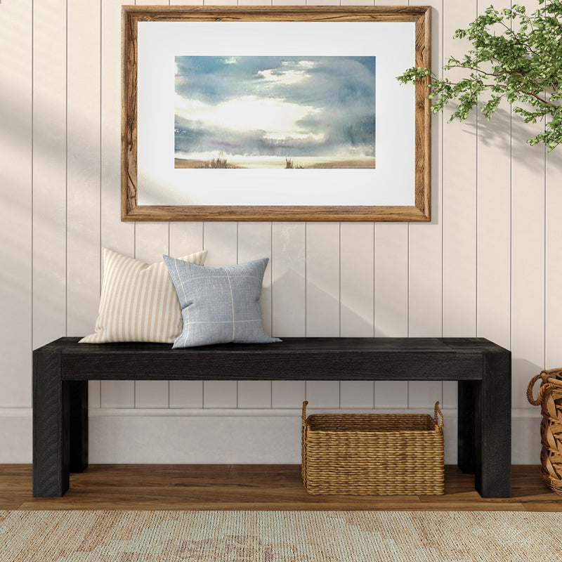 Minimalist entryway with black bench, decorative pillows, framed artwork, and wicker basket on wooden floor.