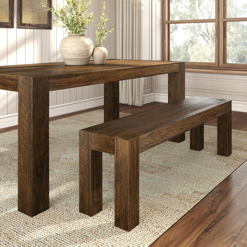 Rustic wooden dining table set with matching bench on textured area rug in bright dining room.