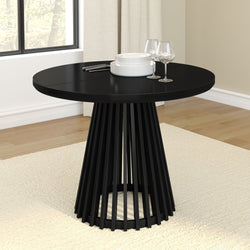 Modern black round dining table with geometric base, set with white plates and wine glasses in a bright dining room.