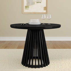 Contemporary black round dining table with a modern design, set with white plates, glassware, and silverware on a wooden floor with an abstract wall art background.