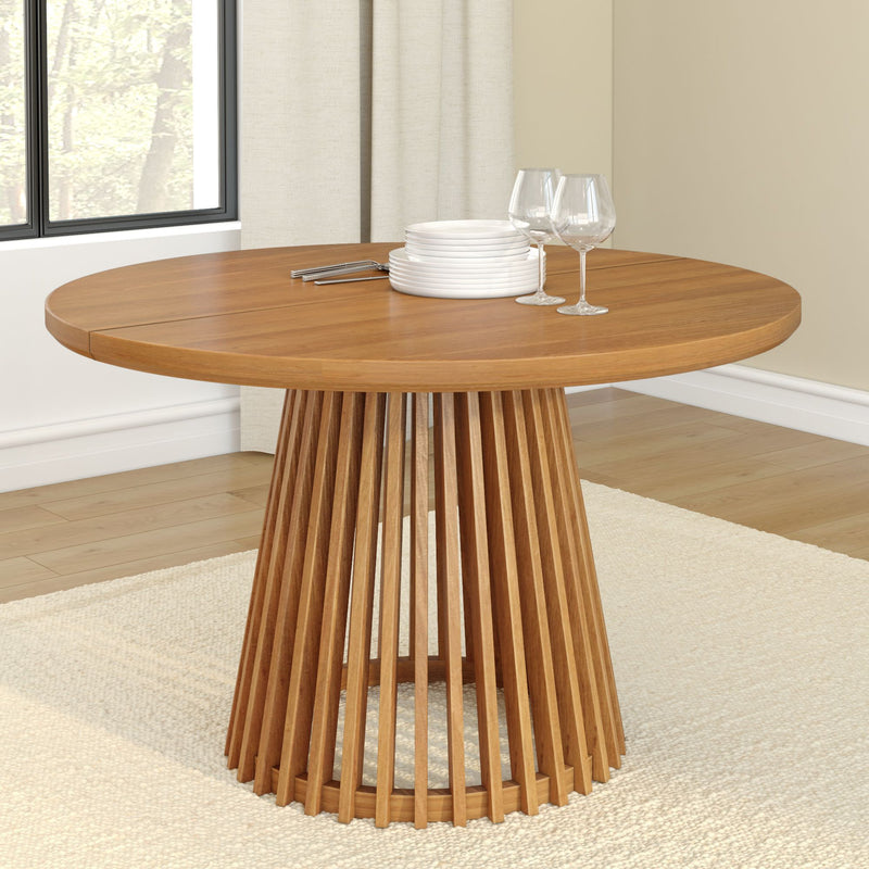 Round wooden dining table with modern slatted base, set with white plates and wine glasses in a bright dining room.