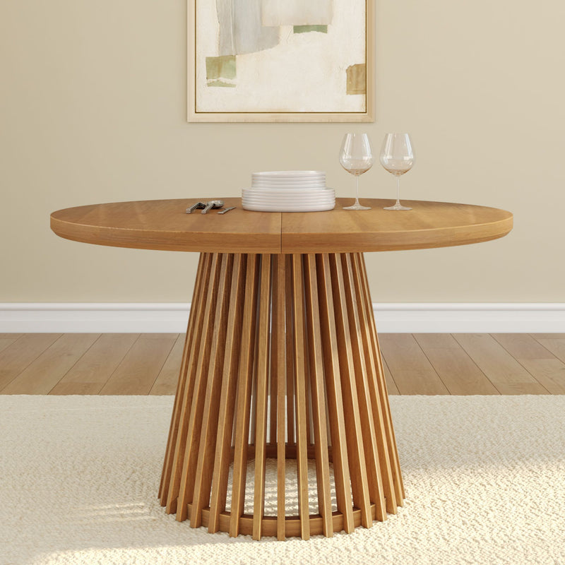 Round wooden dining table with vertical slatted pedestal base, set with plates and wine glasses, in a modern minimalist dining room.