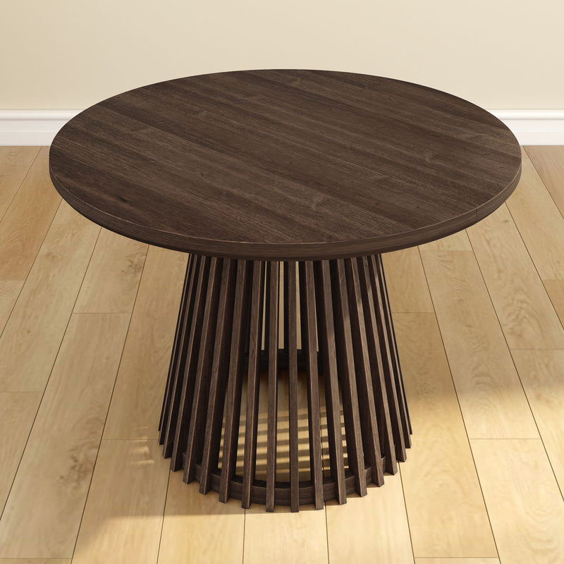 Round wooden dining table with modern slatted base design on hardwood floor.