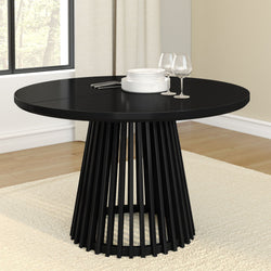 Modern black round dining table with elegant slatted base, set with white plates and wine glasses.