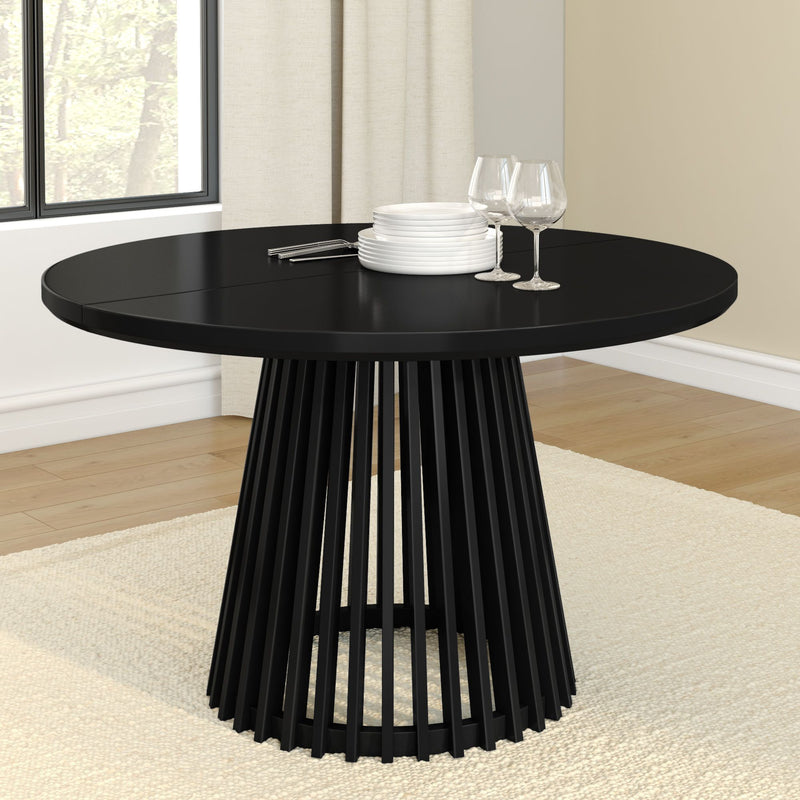 Modern black round dining table with elegant slatted base, set with white plates and wine glasses.