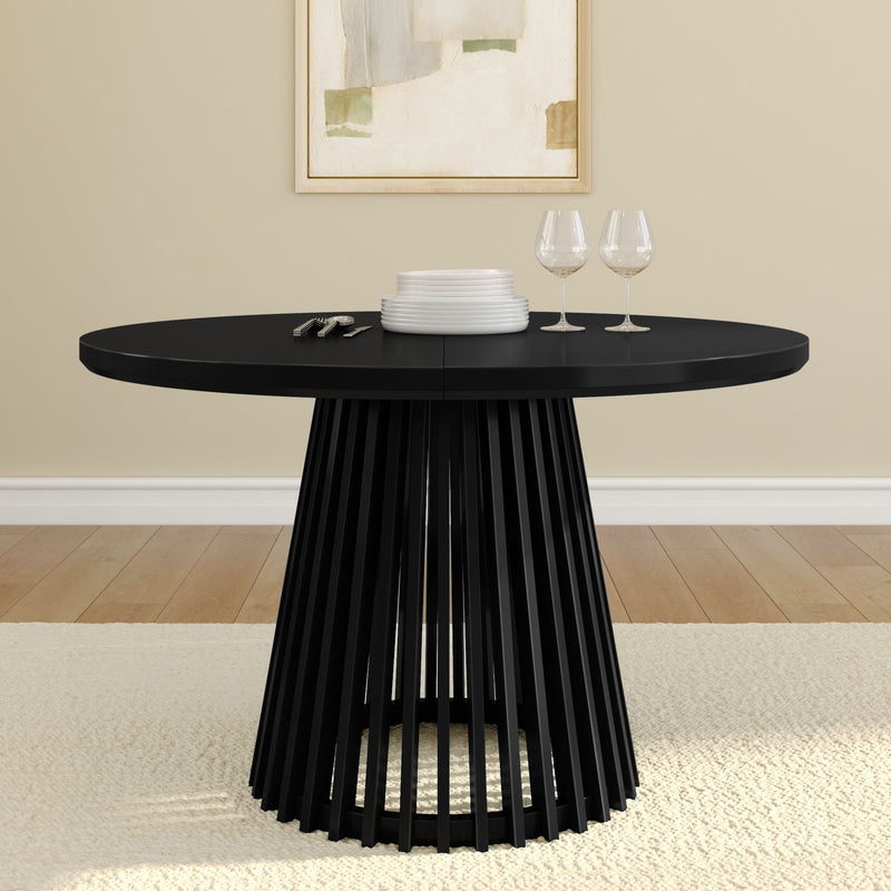 Modern black round dining table with elegant pedestal base, set with white plates and wine glasses in a contemporary dining room.