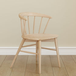 Minimalist wooden chair with a curved backrest on hardwood floor against a beige wall.