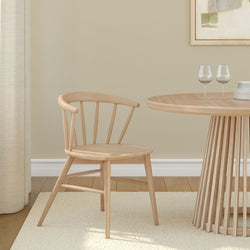Wooden dining chair and round table in minimalist room setting with beige walls.