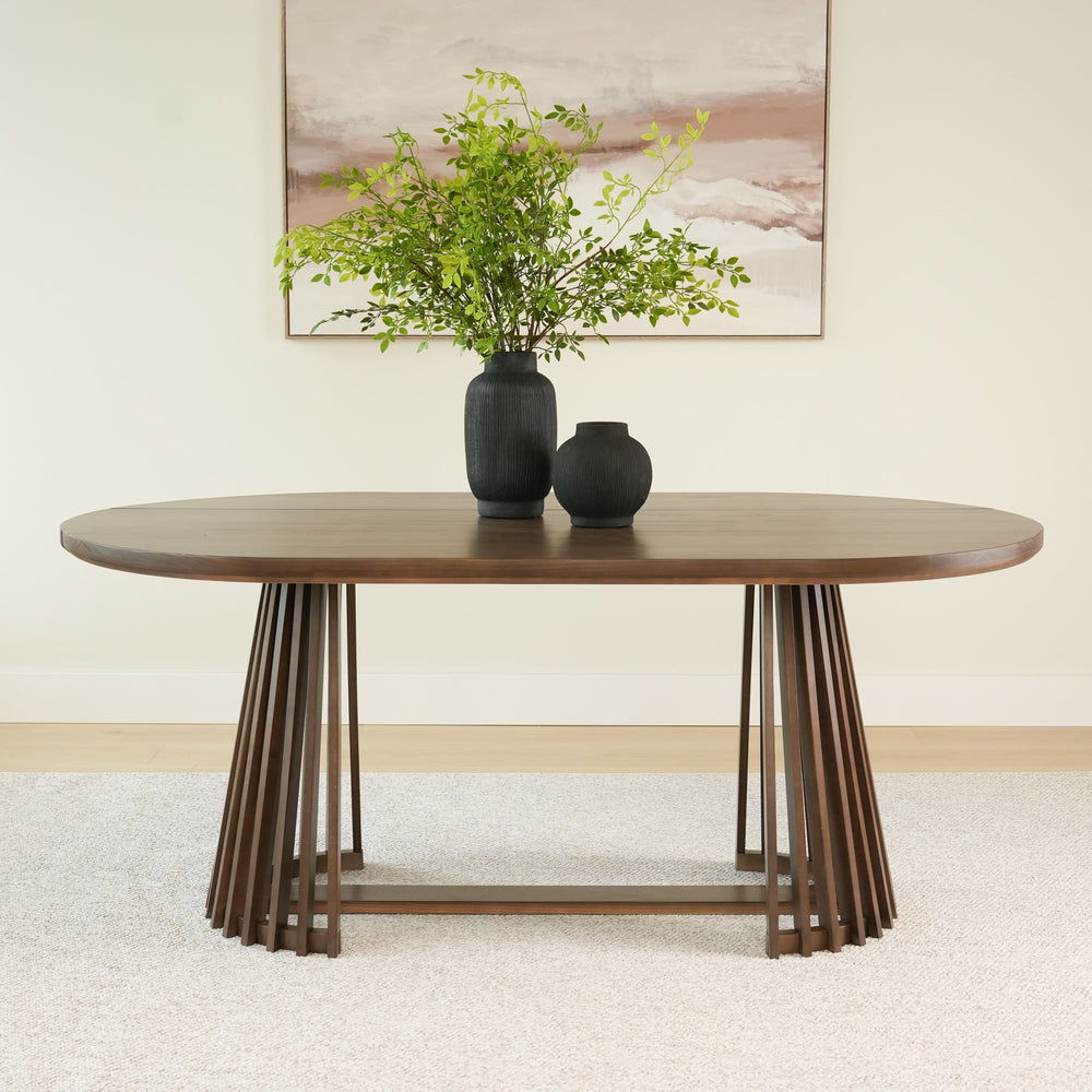 Modern wooden dining table with unique base design and black vases topped with green foliage.