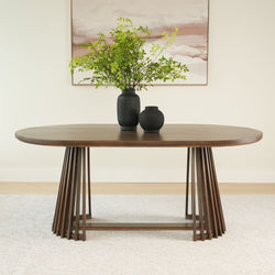 Modern wooden dining table with unique base design and black vases topped with green foliage.