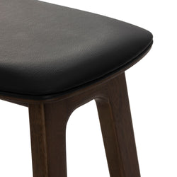 Close-up of black leather upholstered bar stool seat with dark walnut wood legs, modern kitchen counter stool design