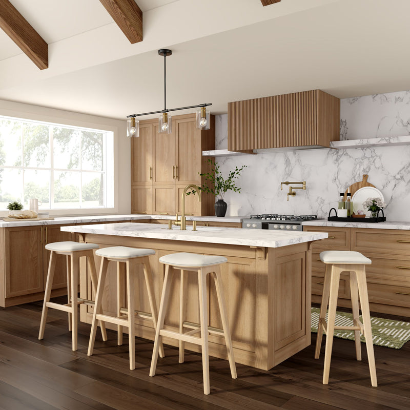 Modern kitchen with light wood cabinetry, marble countertops, and bar stools, featuring a large window and pendant lighting.
