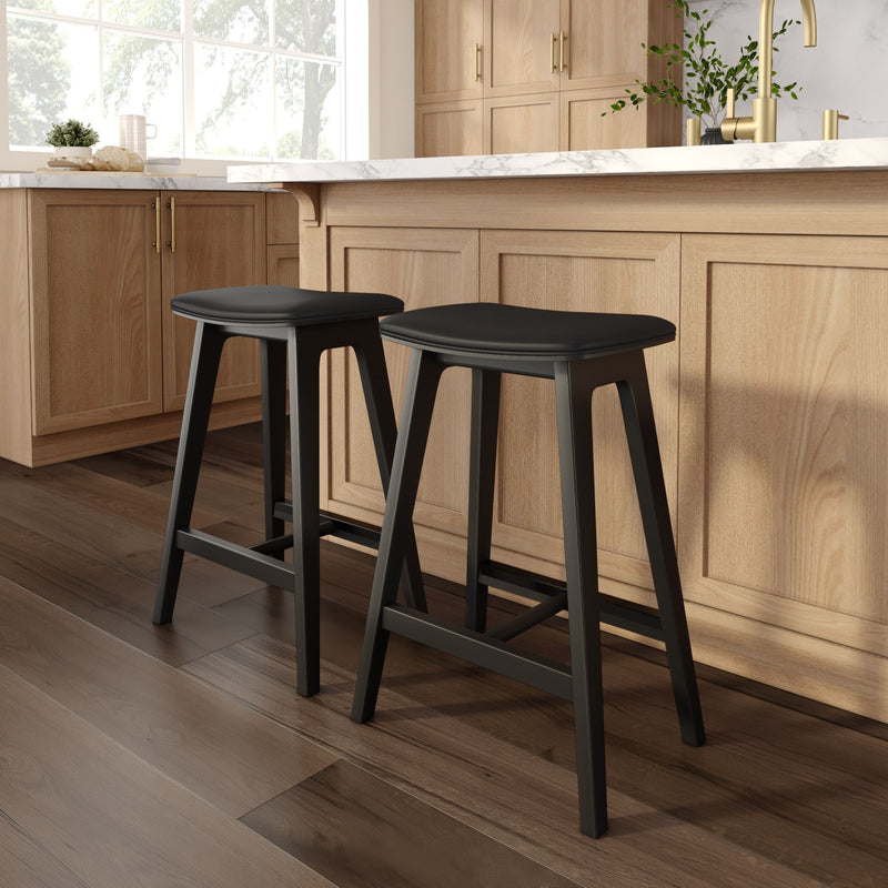 Pair of modern black counter stools at oak kitchen island with white marble countertop, brass faucet and dark hardwood floors
