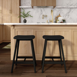 Contemporary kitchen island with light oak cabinets, white marble countertop, brass faucet, two black bar stools, wood flooring and decorative plant.