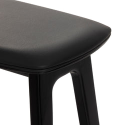 Close-up of black leather padded bar stool seat with rounded edge and black wooden leg, modern minimalist kitchen counter stool