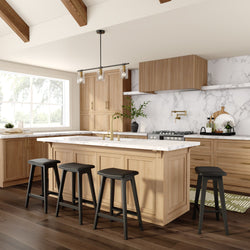 Modern farmhouse kitchen with light wood cabinets, marble countertops and backsplash, large island with brass faucet, black bar stools, pendant lighting and hardwood floors.