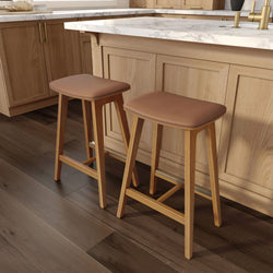 Two wooden bar stools with cushioned seats in a modern kitchen with marble countertop.