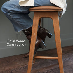 Solid wood counter stool with leather cushion and footrest in warm wood finish, model wearing jeans and brown leather heeled boots