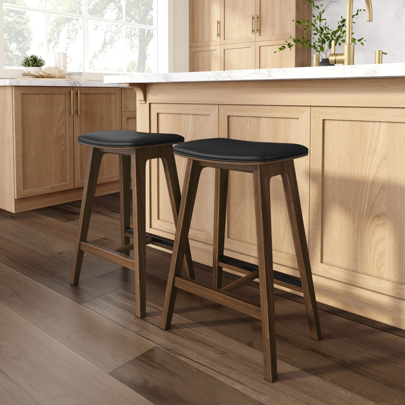 Two modern walnut counter-height bar stools with black leather cushions at a light wood kitchen island with white marble countertop, brass faucet, and hardwood floors.