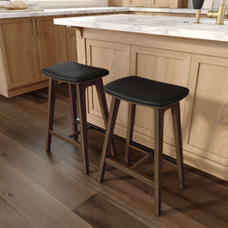 Modern kitchen island with white marble countertop, light oak cabinets, brass faucet, and two black leather bar stools on dark hardwood floors