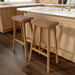 Wooden kitchen stools with cushioned seats alongside a marble island in a modern kitchen setting.