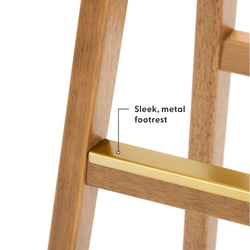 Close-up of warm wood finish bar stool leg with gold-tone metal footrest, modern mid-century style bar stool detail