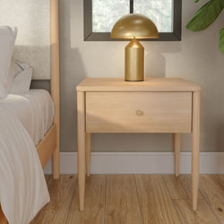Minimalist light wood nightstand with single drawer and gold mushroom table lamp beside bed with white linens on oak floor
