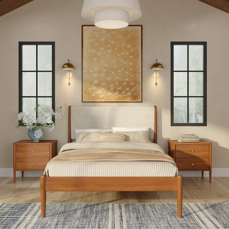 Mid-century modern bedroom interior with wooden bed frame and upholstered headboard, matching wooden nightstands, brass wall sconces, large framed bird artwork, striped neutral bedding, hardwood floor, area rug, tall black-framed windows and vase of white flowers