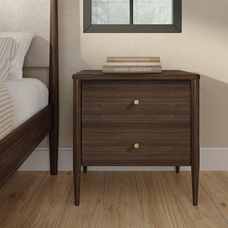 Walnut nightstand mid-century modern two-drawer bedside table with brass knobs next to upholstered bed on oak hardwood floor with stacked books and window in minimalist bedroom