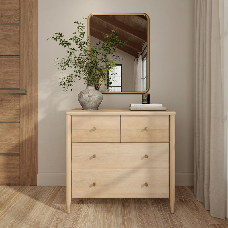 Minimalist light wood dresser with brass knobs, rectangular mirror, ceramic vase of greenery and stacked books in neutral modern bedroom decor