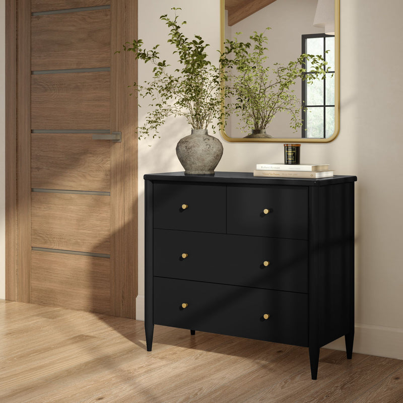 Modern black four-drawer dresser with gold knobs in a bright entryway, wooden door, wall mirror, rustic vase with greenery and hardwood floor