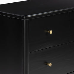 Close-up of a modern black wooden dresser with matte finish and gold brass knobs, showing rounded corner and drawer details