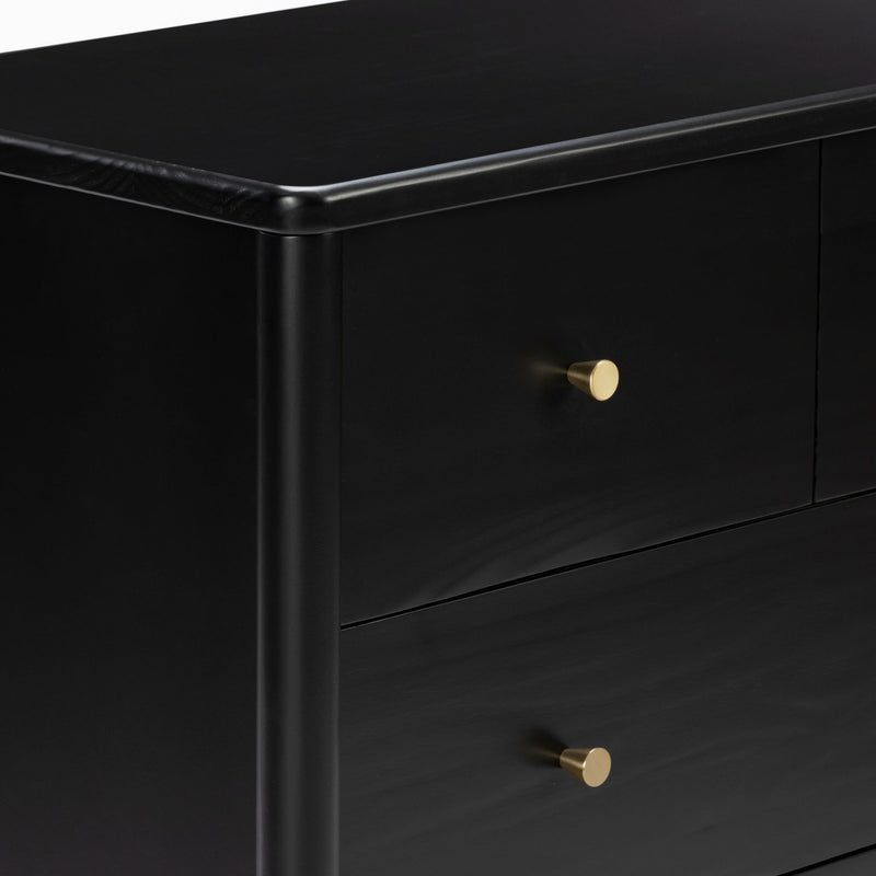 Close-up of a modern black wooden dresser with matte finish and gold brass knobs, showing rounded corner and drawer details