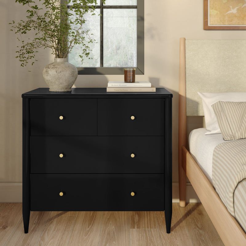 Modern black 4-drawer dresser with brass knobs beside a light wood bed, styled with a rustic stone vase, stacked books and candle in a contemporary bedroom with hardwood floors