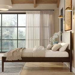 Modern cozy Scandinavian bedroom with dark wood platform bed, neutral linen bedding, striped throw, and large grid window overlooking forest
